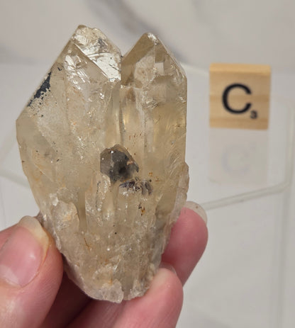 citrine cluster specimen being held in a hand with a wooden letter tile in the background against a white marbled background