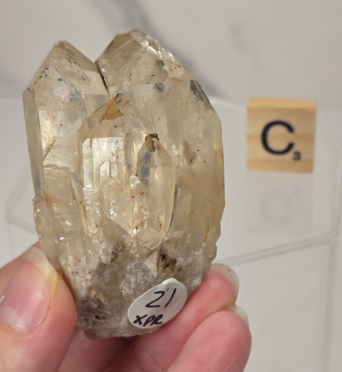 citrine cluster specimen being held in a hand with a wooden letter tile in the background against a white marbled background