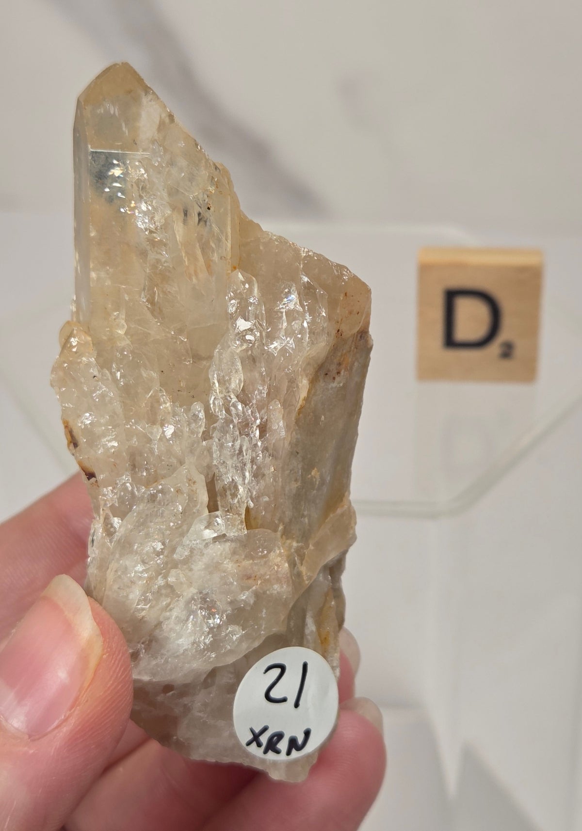citrine cluster specimen being held in a hand with a wooden letter tile in the background against a white marbled background
