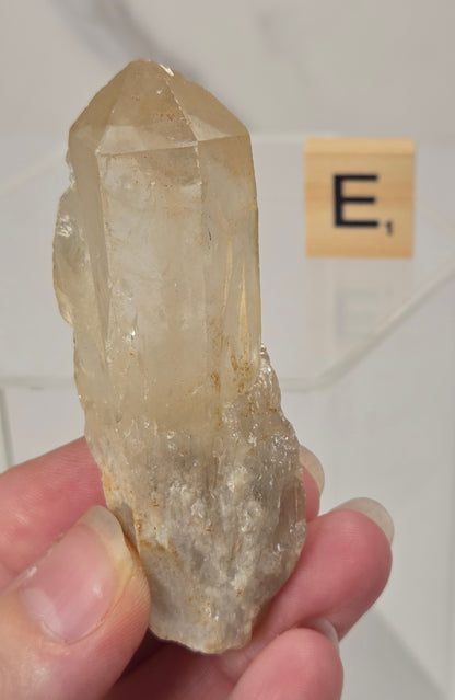 citrine cluster specimen being held in a hand with a wooden letter tile in the background against a white marbled background