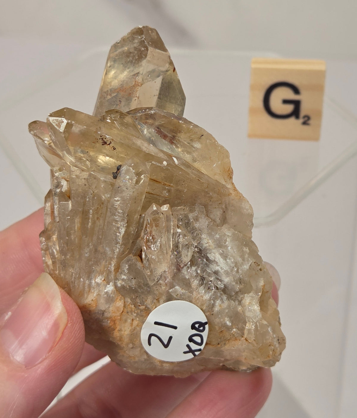 citrine cluster specimen being held in a hand with a wooden letter tile in the background against a white marbled background