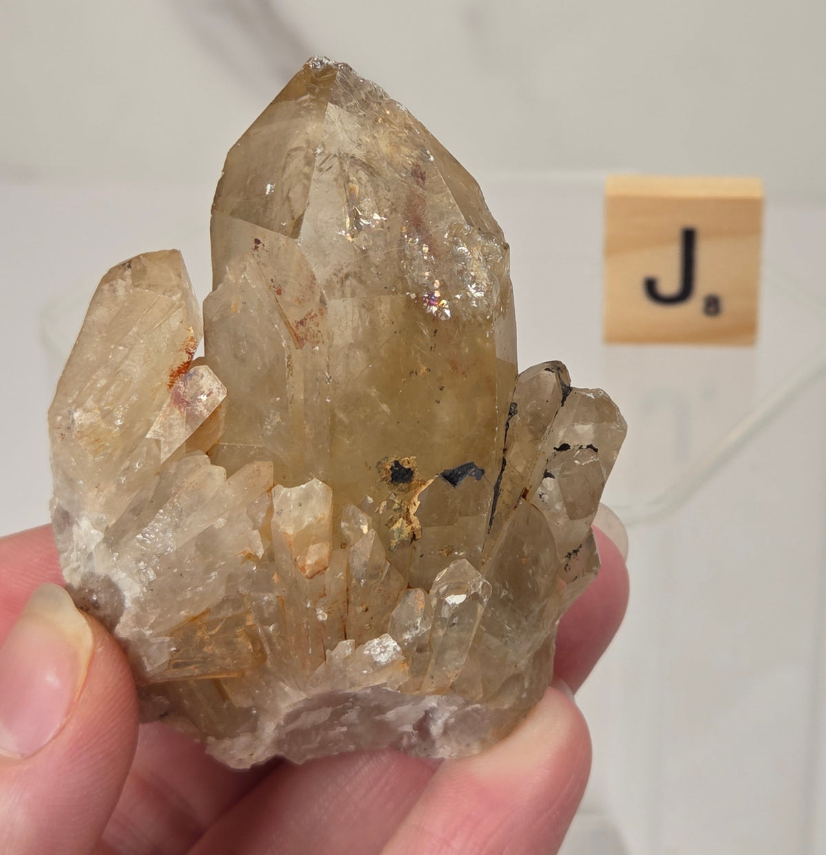 citrine cluster specimen being held in a hand with a wooden letter tile in the background against a white marbled background
