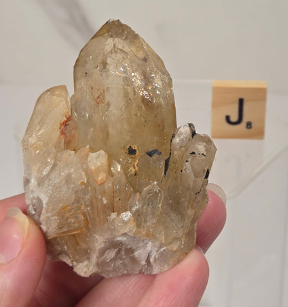 citrine cluster specimen being held in a hand with a wooden letter tile in the background against a white marbled background