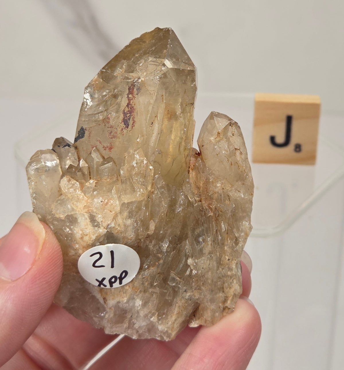 citrine cluster specimen being held in a hand with a wooden letter tile in the background against a white marbled background