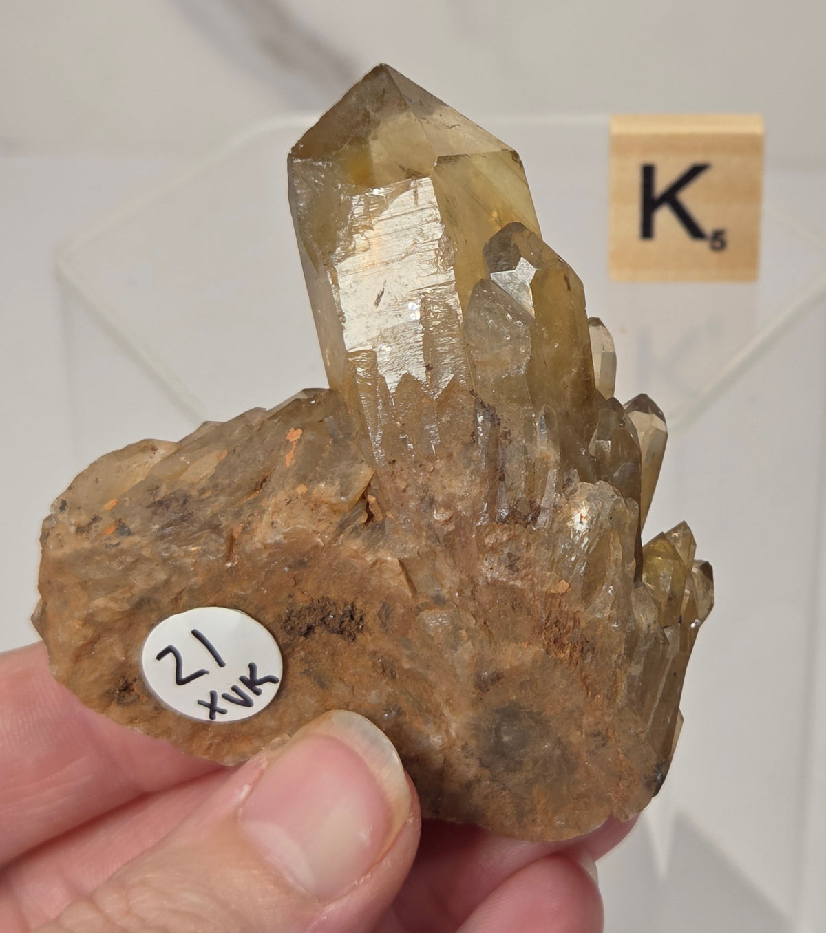 citrine cluster specimen being held in a hand with a wooden letter tile in the background against a white marbled background