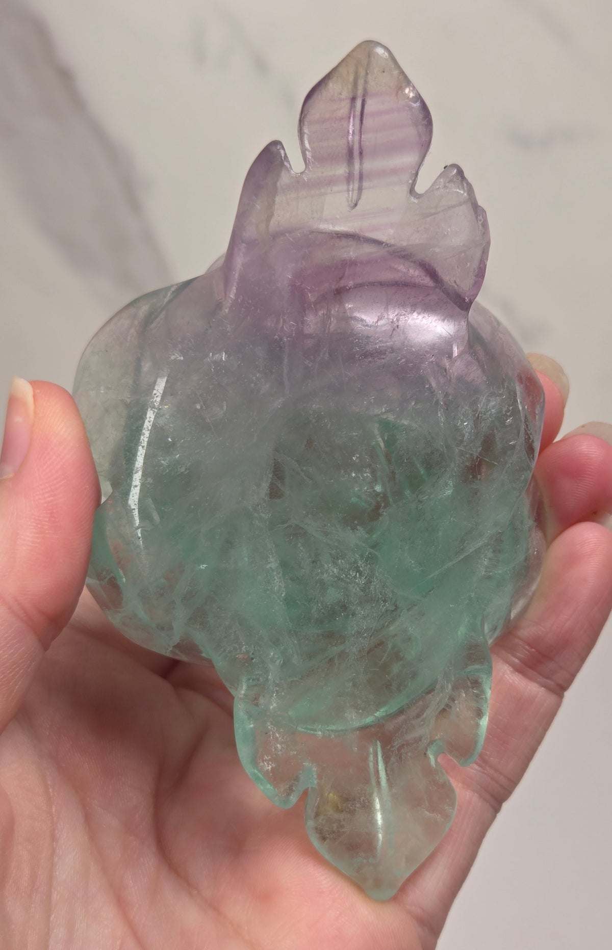 A carved rose-shaped decorative object made of translucent stone with a color gradient from light aqua blue to soft lavender-pink, against a plain light background.