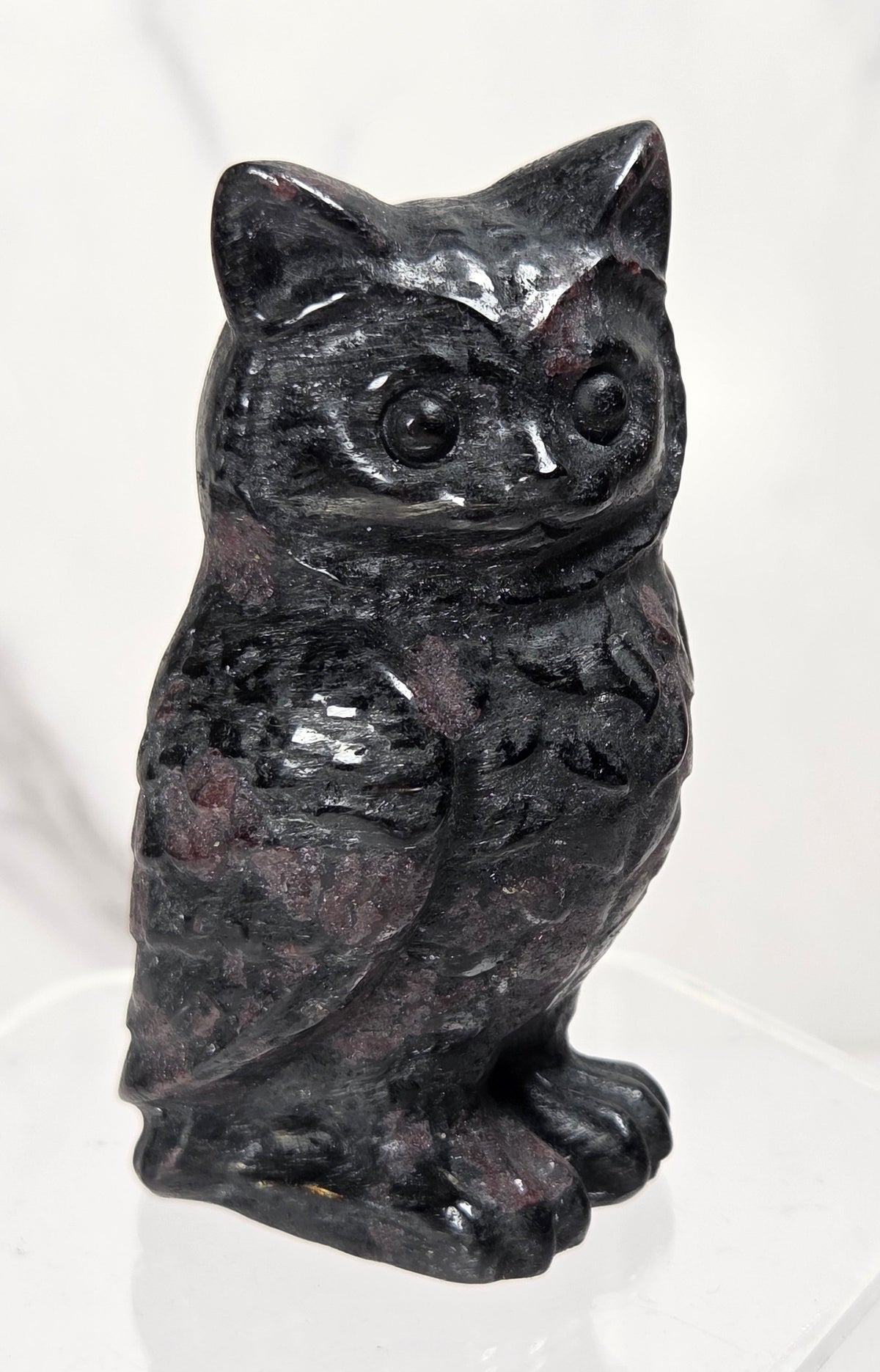 A small carved stone owl figurine with a mottled dark gray and white pattern, standing upright on a plain light surface.