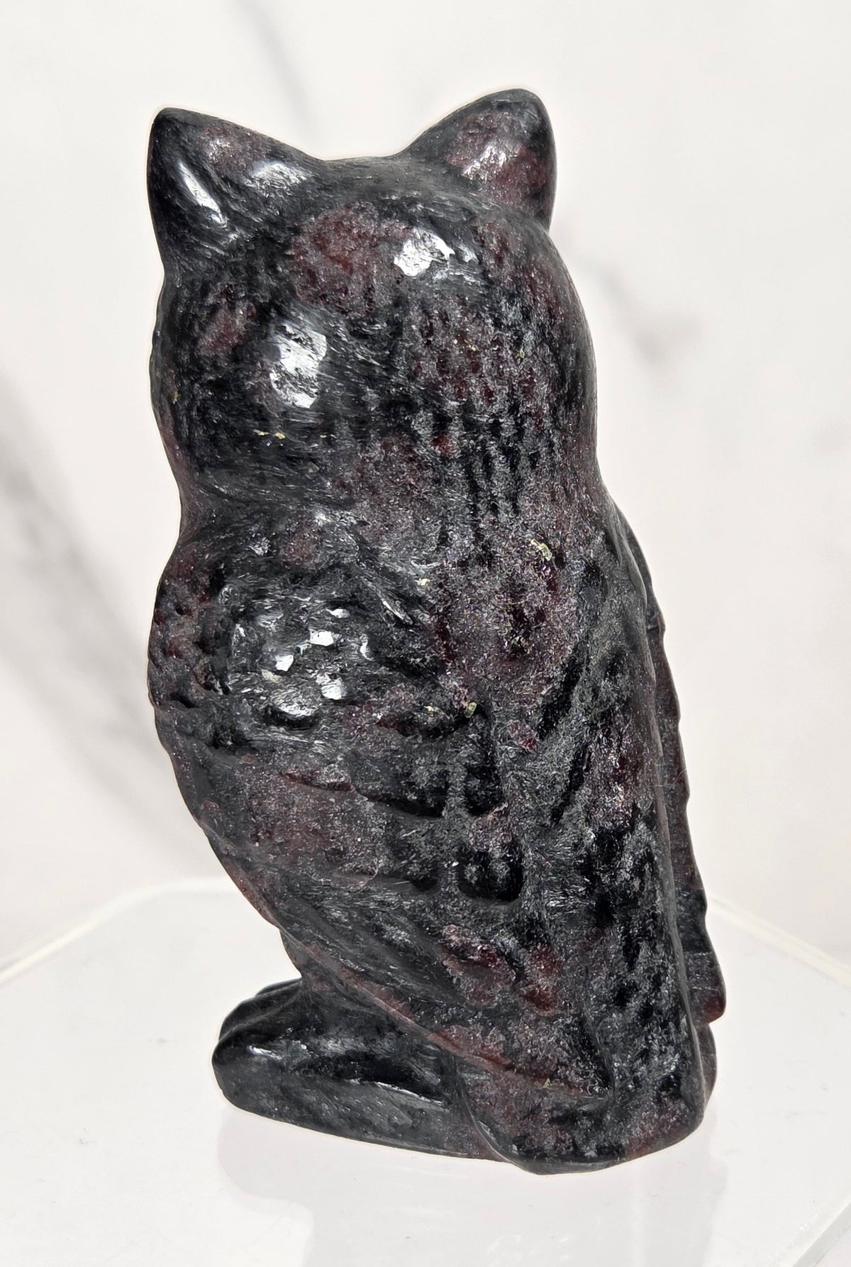 A small carved stone owl figurine with a mottled dark gray and white pattern, standing upright on a plain light surface.