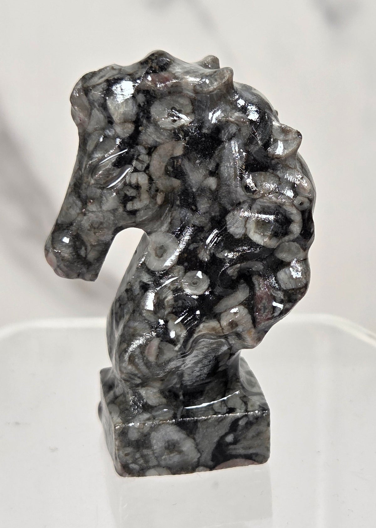 A small carved horse head figurine made of black and white marbled stone, displayed on a clear acrylic stand against a light marble-patterned background.