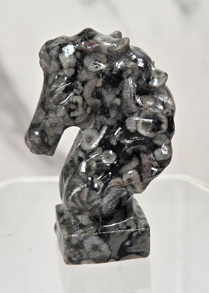 A small carved horse head figurine made of black and white marbled stone, displayed on a clear acrylic stand against a light marble-patterned background.