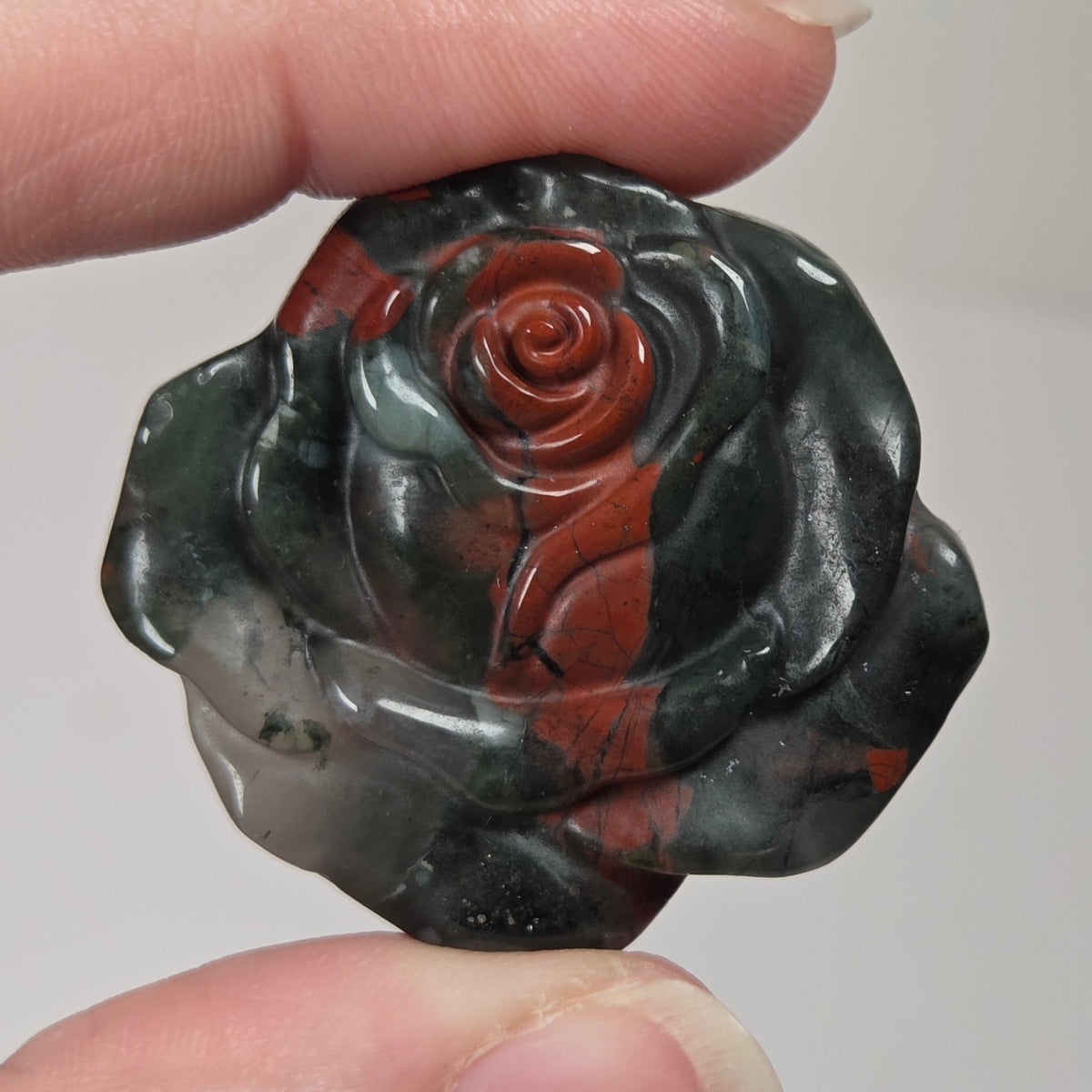 Black and red stone carving of a rose shape being held in a hand against a white background