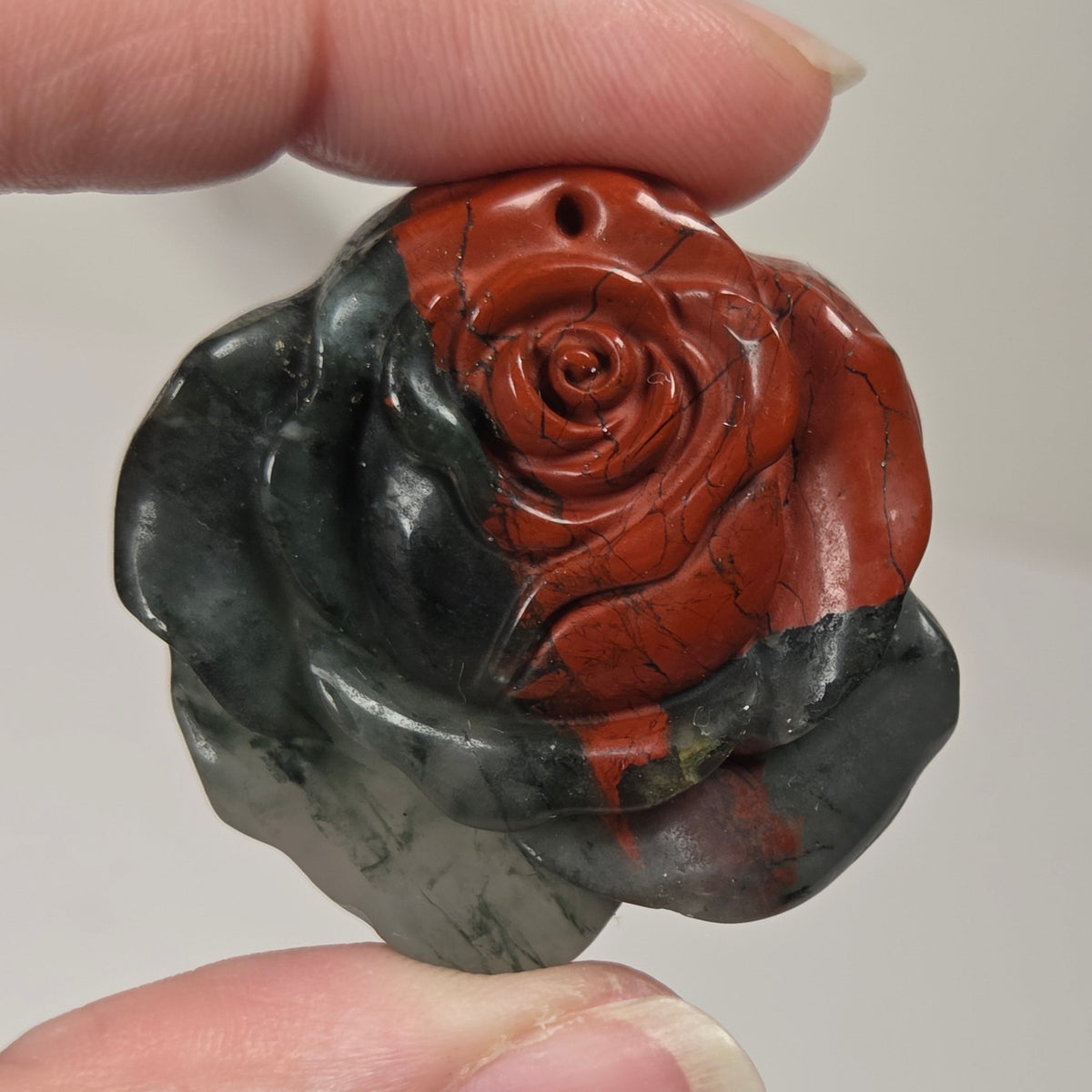 Black and red stone carving of a rose shape being held in a hand against a white background