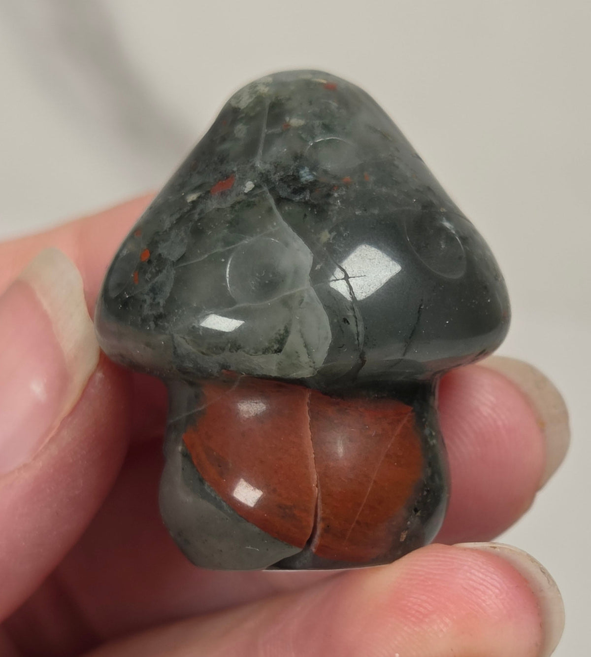 Small toadstool stone carving with black, grey and red coloring being held in a hand held against a white background