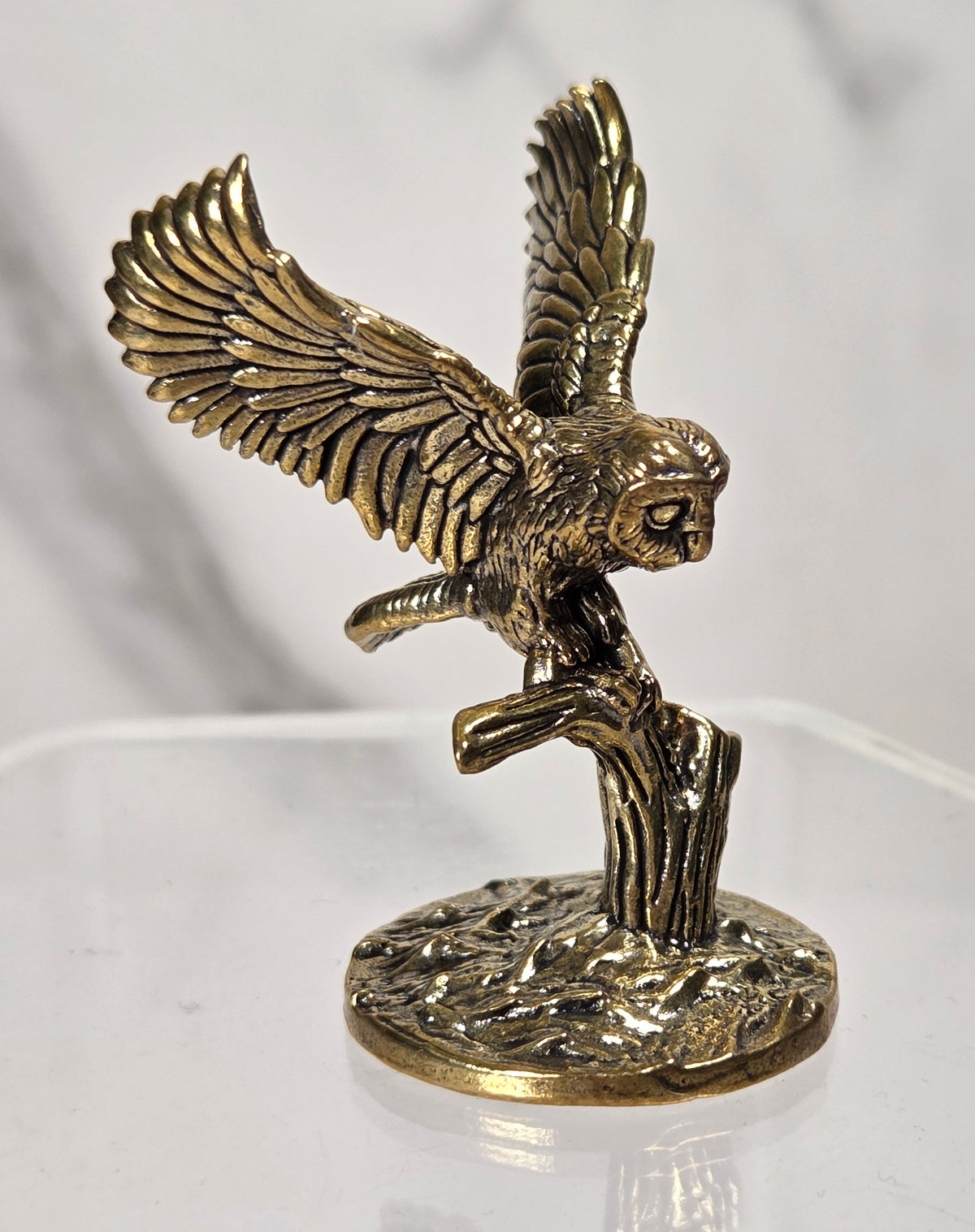 A small antique-style metal figurine of an owl on a branch displayed on a clear acrylic stand.
