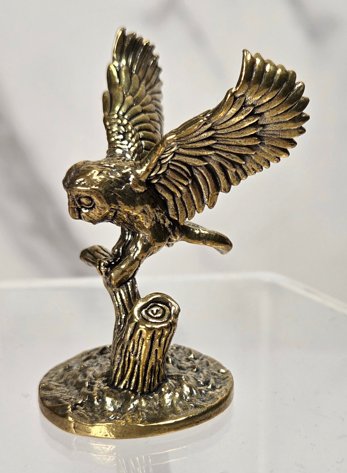 A small antique-style metal figurine of an owl on a branch displayed on a clear acrylic stand.