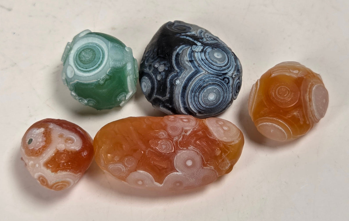 Specimens called gobi agate in orange, green and black coloring with orbicular patterns on a white background