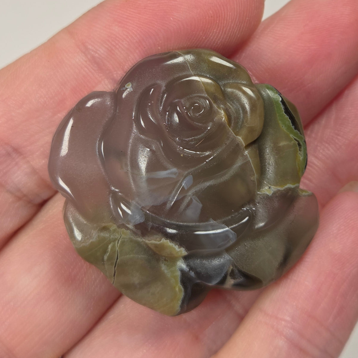 Tan and translucent stone carving of a rose shape being held in a hand against a white background