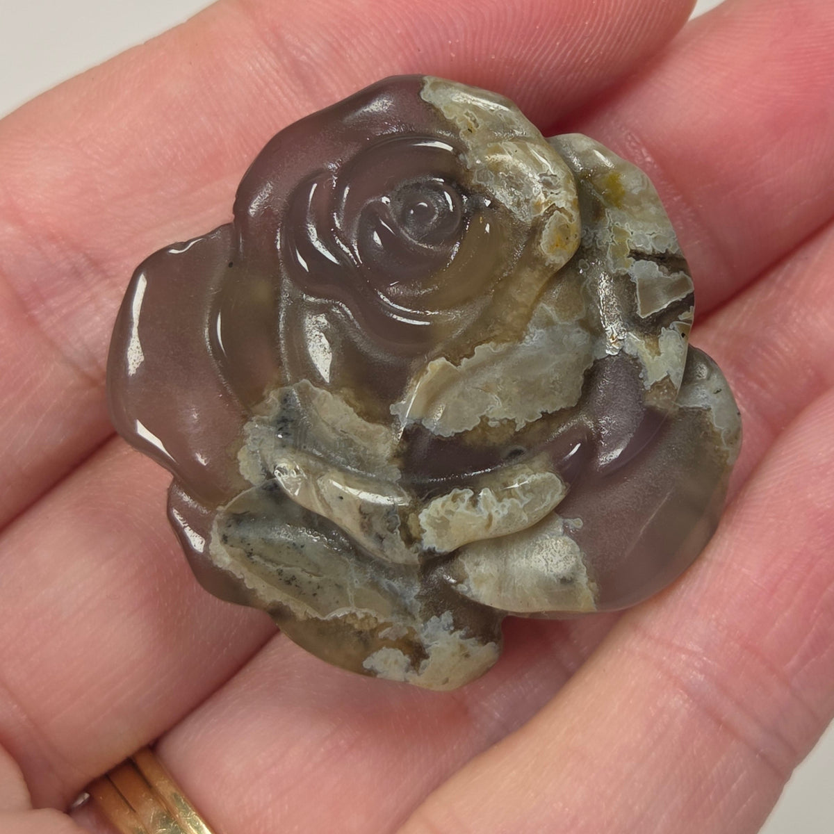 Tan and translucent stone carving of a rose shape being held in a hand against a white background