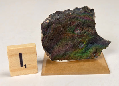 An iridescent mineral or stone sample displayed on a small wooden stand, next to a small wooden block marked with the number 1, on a plain off-white background.