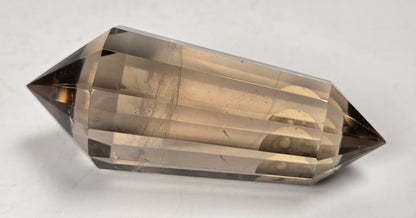 A faceted smoky quartz crystal point, showing a translucent light brown to dark brown gradient, photographed on a neutral light gray surface.