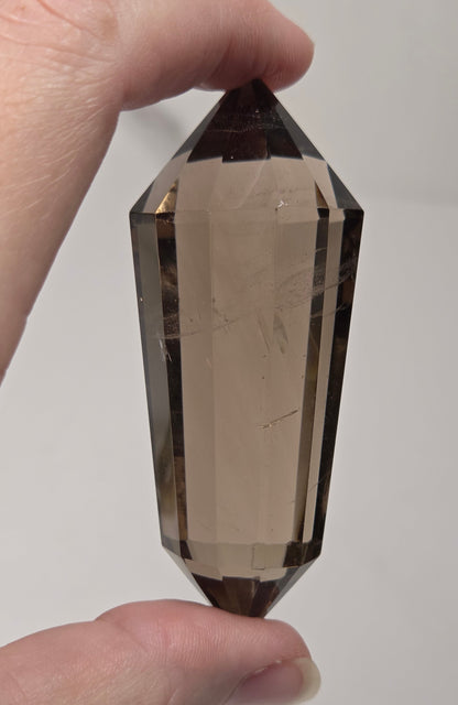 A hand holding a faceted smoky quartz crystal point against a plain light gray background.