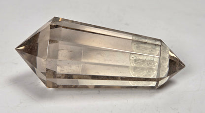 A faceted clear quartz crystal point, also known as a smoky quartz crystal, resting on a plain white surface.