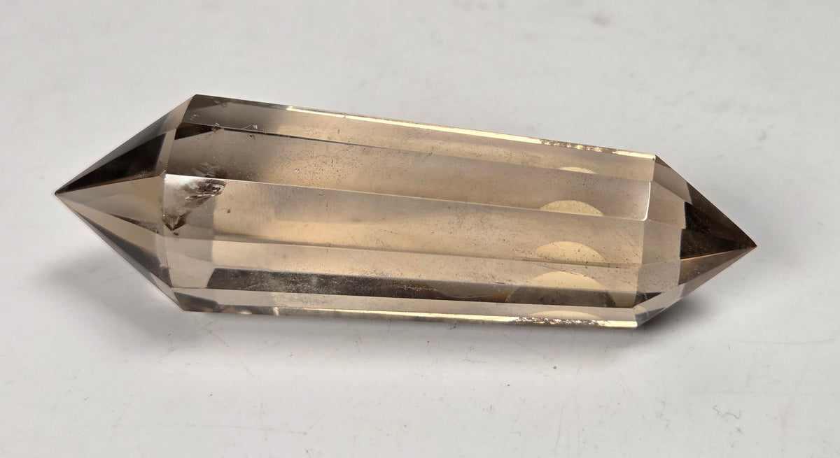 A natural smoky quartz crystal point with a double-tip structure, resting on a plain light gray surface.