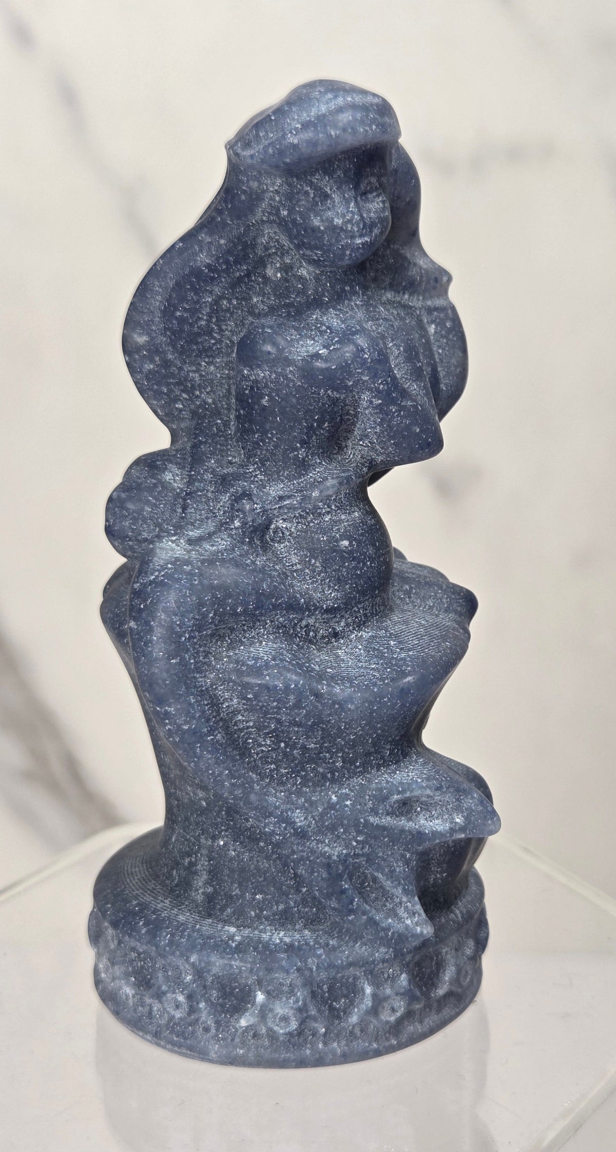 mermaid carving made of blue aventurine similar to the disney princess ariel on an acrylic shelf against a white background