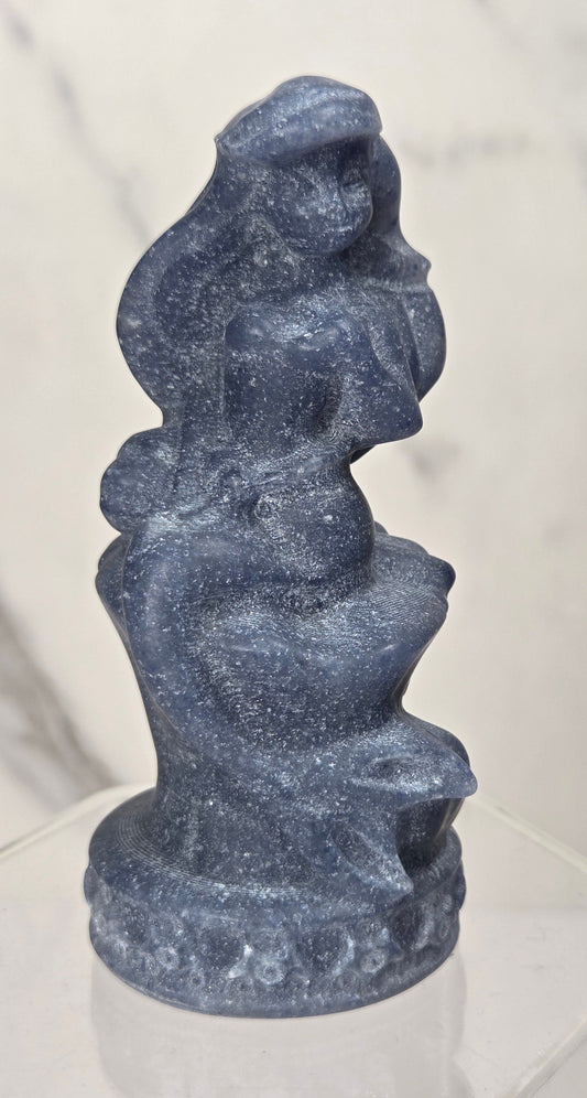 mermaid carving made of blue aventurine similar to the disney princess ariel on an acrylic shelf against a white background