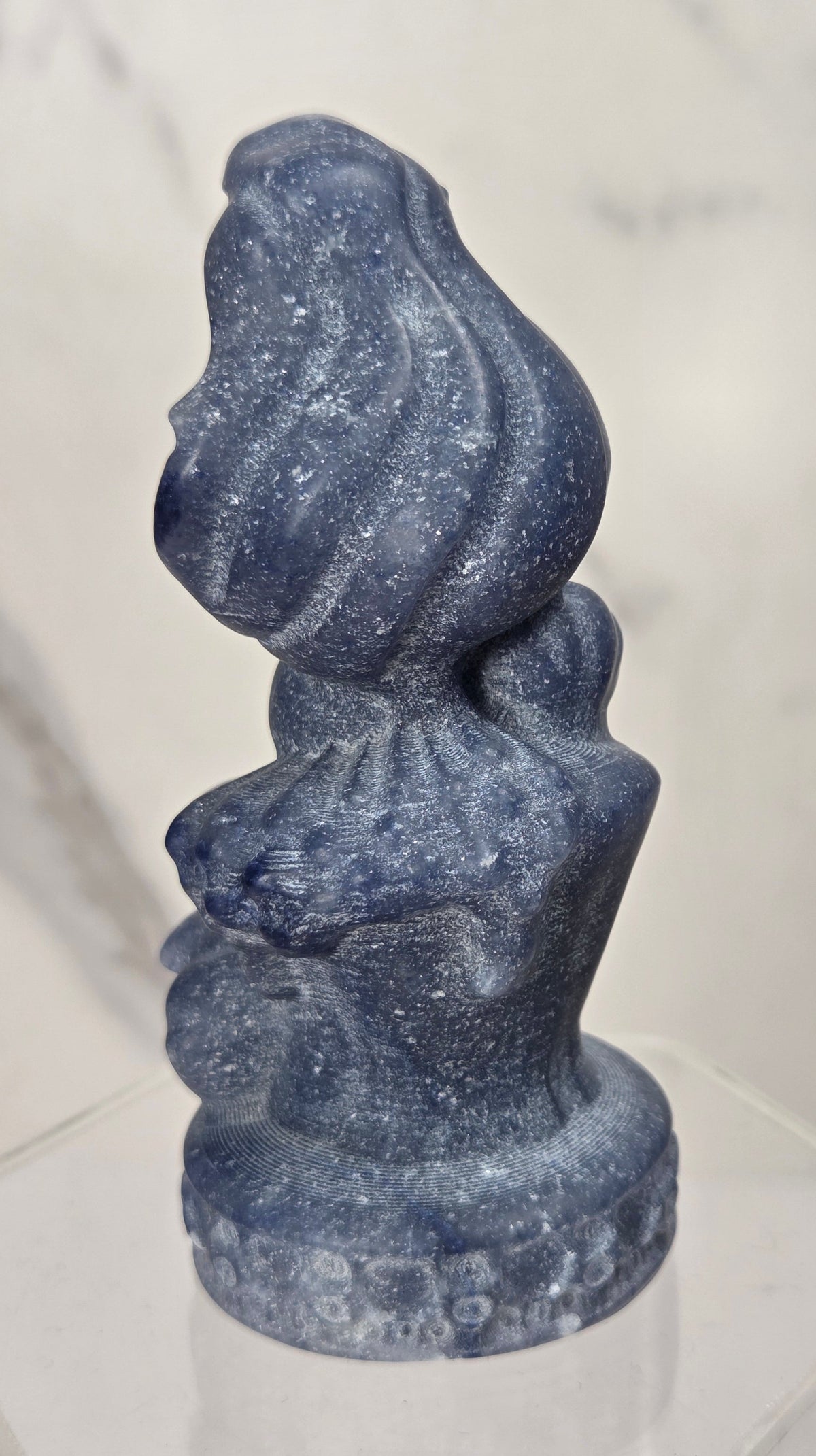 mermaid carving made of blue aventurine similar to the disney princess ariel on an acrylic shelf against a white background