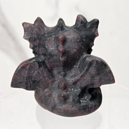 A small black and red crystal dragon figurine with large black eyes, sitting on a clear acrylic display stand against a light marble-patterned background.
