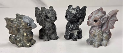 Collection of small carved figurines of a stylized animal, likely a dragon, made from various color and material stones, photographed on a plain light background.