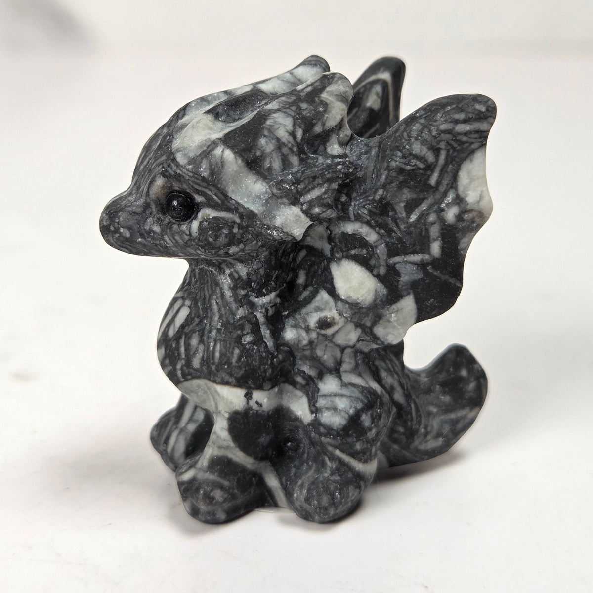 A small carved figurine of a dragon or fantasy creature made from black and white marbled stone, standing on a light surface with a soft blurred background.