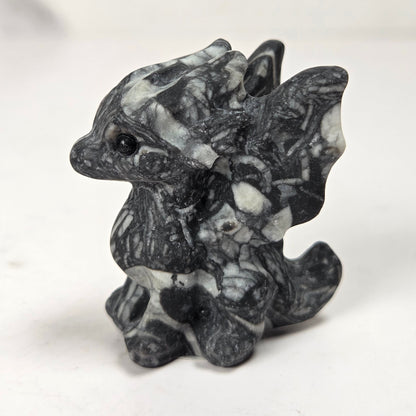 A small carved figurine of a dragon or fantasy creature made from black and white marbled stone, standing on a light surface with a soft blurred background.