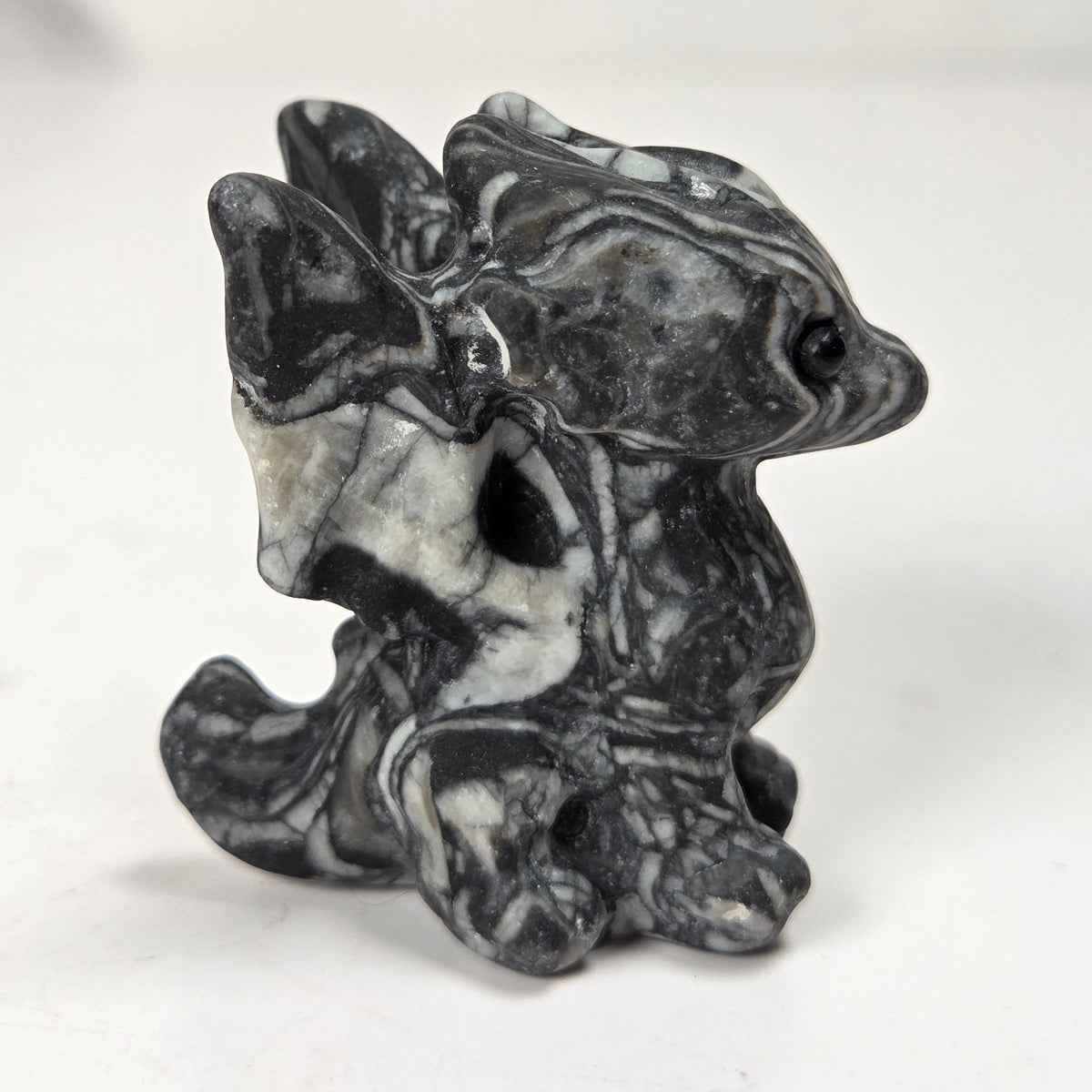 A small carved figurine of a dragon or fantasy creature made from black and white marbled stone, standing on a light surface with a soft blurred background.
