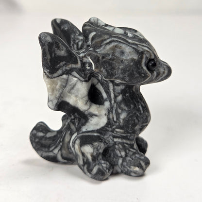 A small carved figurine of a dragon or fantasy creature made from black and white marbled stone, standing on a light surface with a soft blurred background.