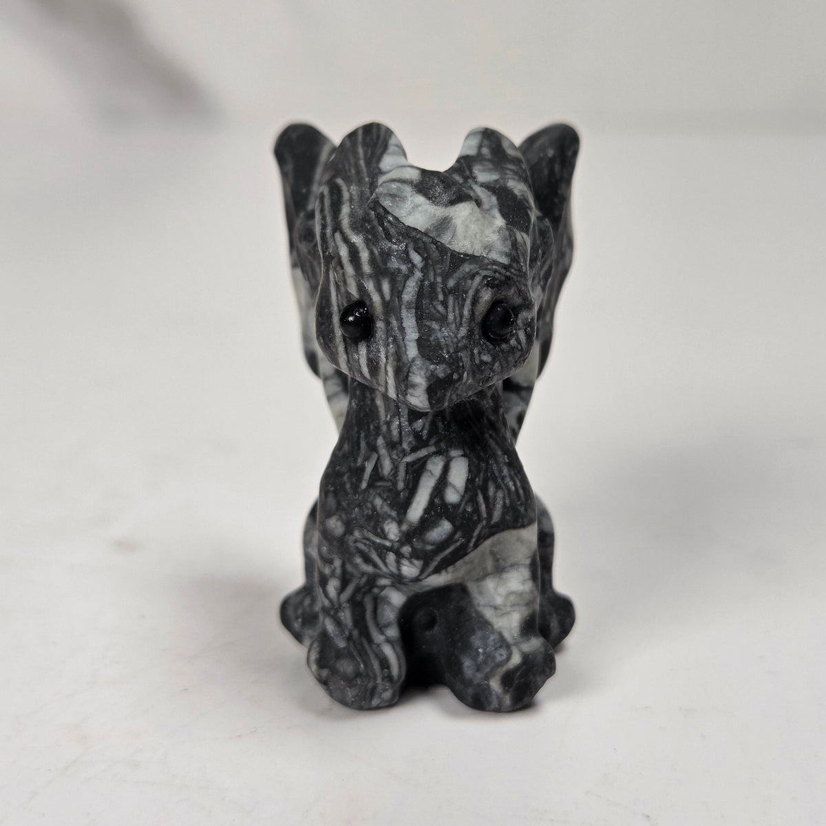 A small carved figurine of a dragon or fantasy creature made from black and white marbled stone, standing on a light surface with a soft blurred background.