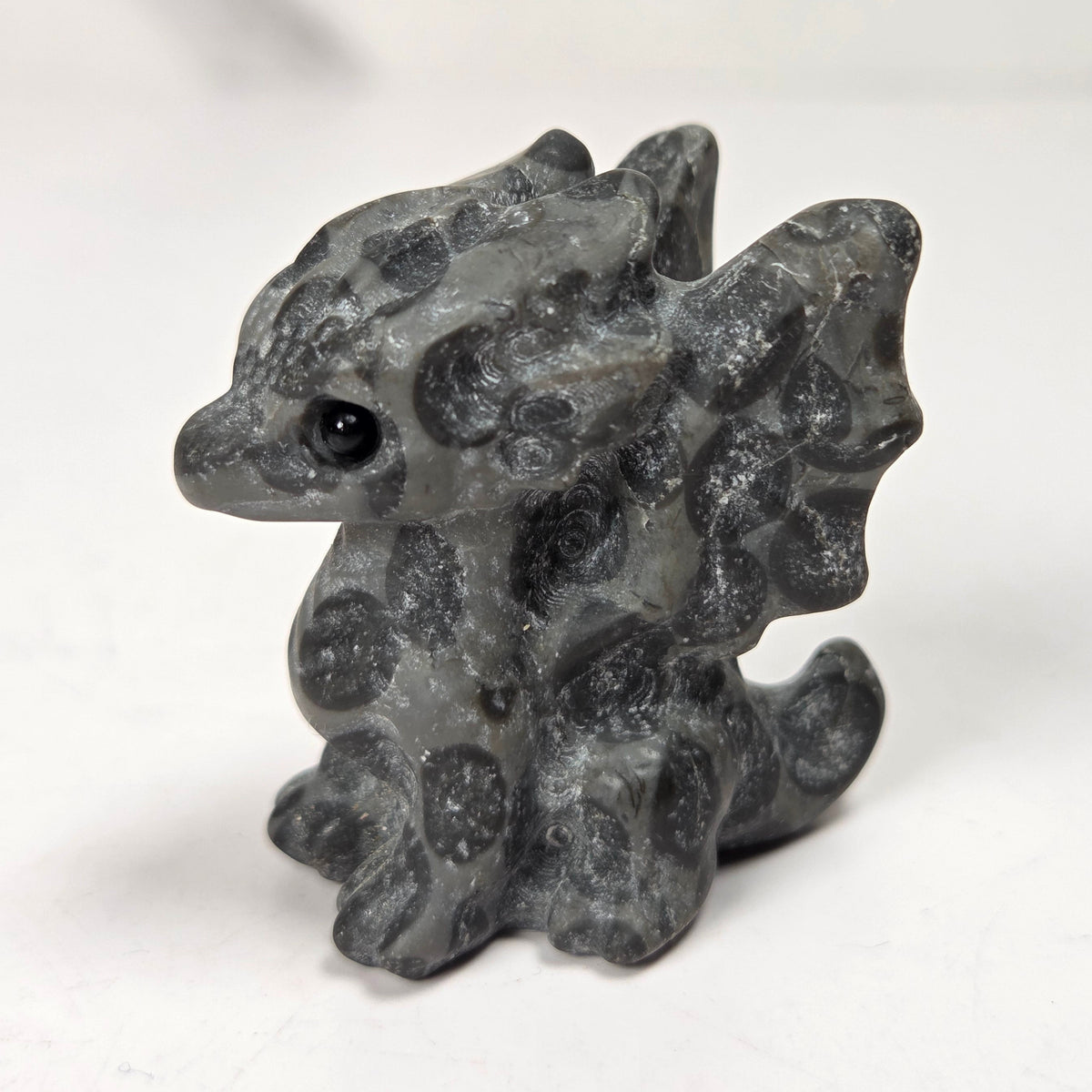 A small carved figurine of a dragon or fantasy creature made from black and white marbled stone, standing on a light surface with a soft blurred background.
