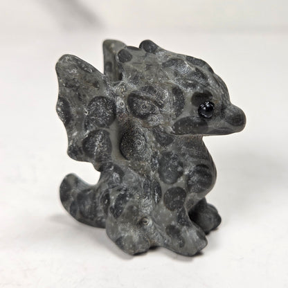 A small carved figurine of a dragon or fantasy creature made from black and white marbled stone, standing on a light surface with a soft blurred background.