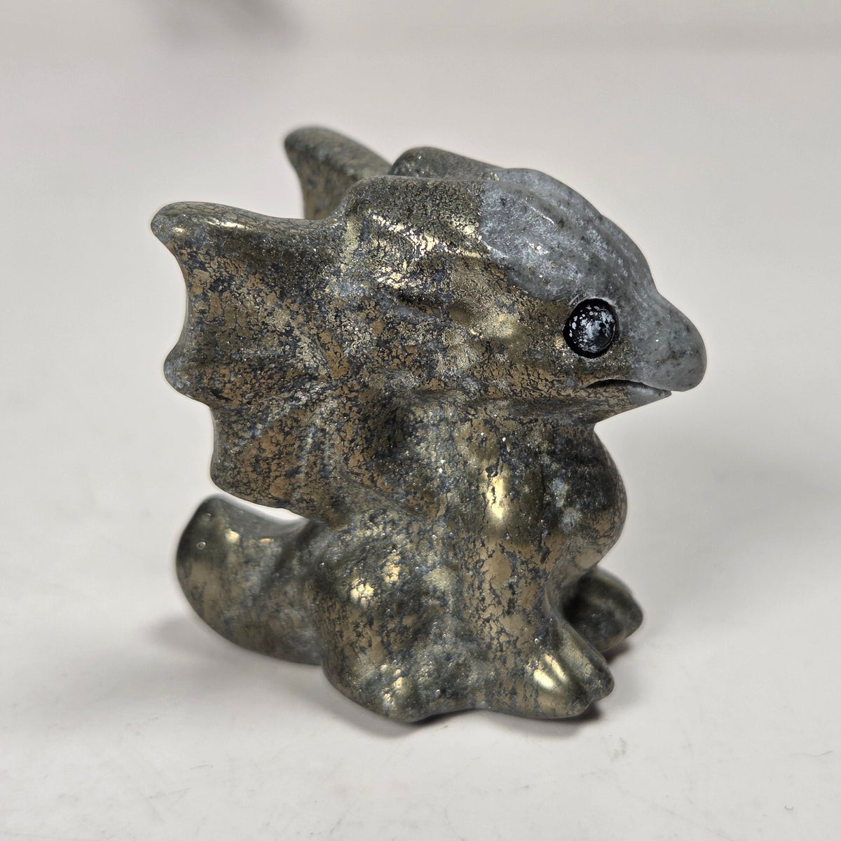 A small carved figurine of a dragon or fantasy creature made from pyrite stone, standing on a light surface with a soft blurred background.