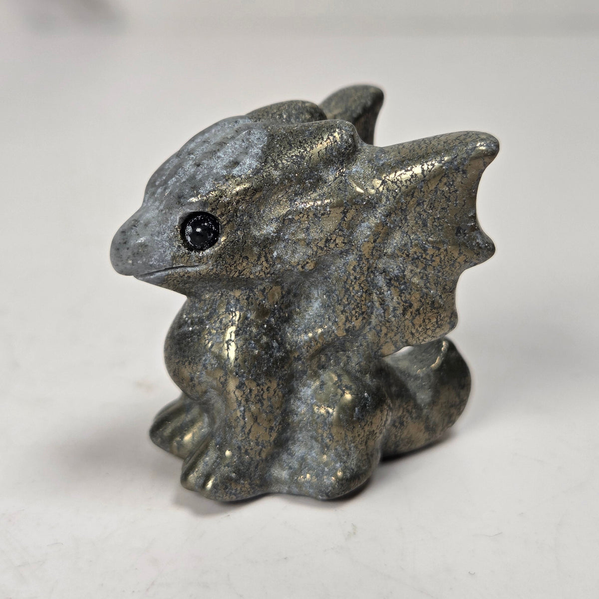 A small carved figurine of a dragon or fantasy creature made from pyrite stone, standing on a light surface with a soft blurred background.
