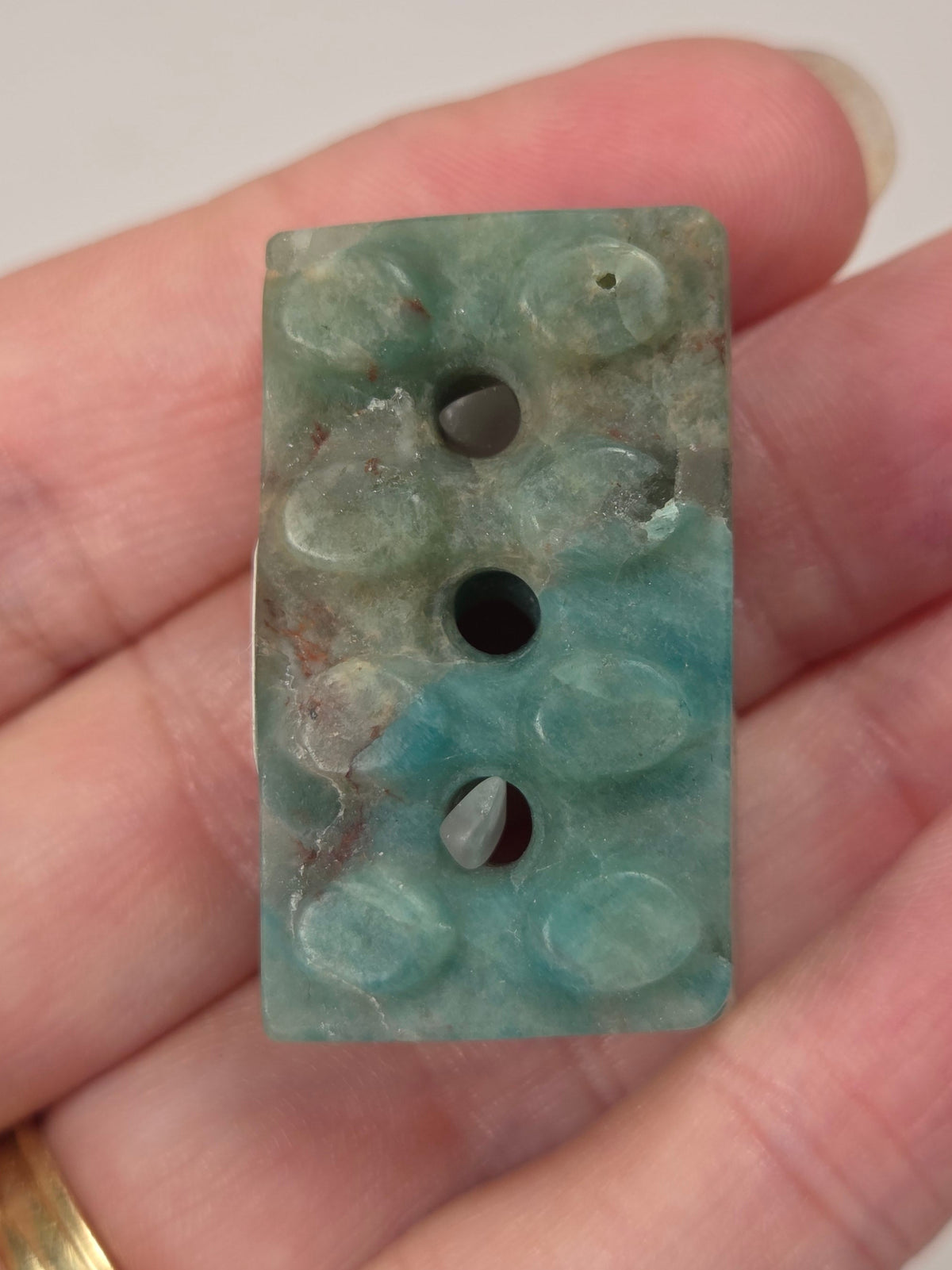 Crystal brick style carving with blue coloring being held in a hand against a white background