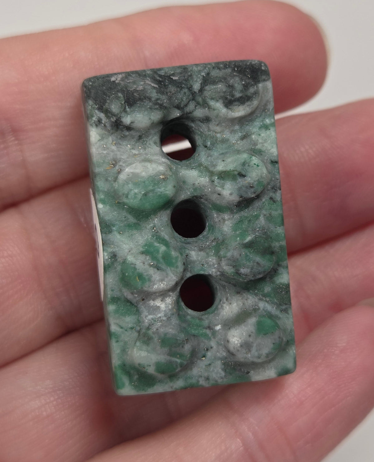 Crystal brick style carving with green, white, and black coloring being held in a hand against a white background