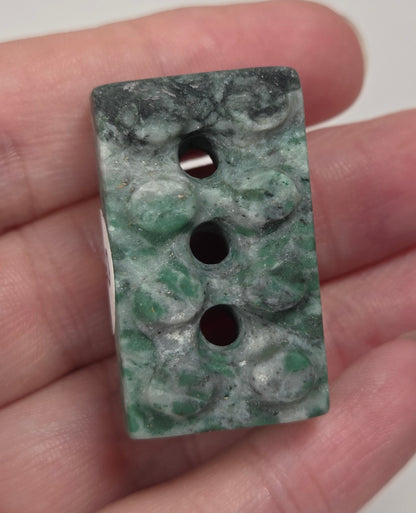 Crystal brick style carving with green, white, and black coloring being held in a hand against a white background