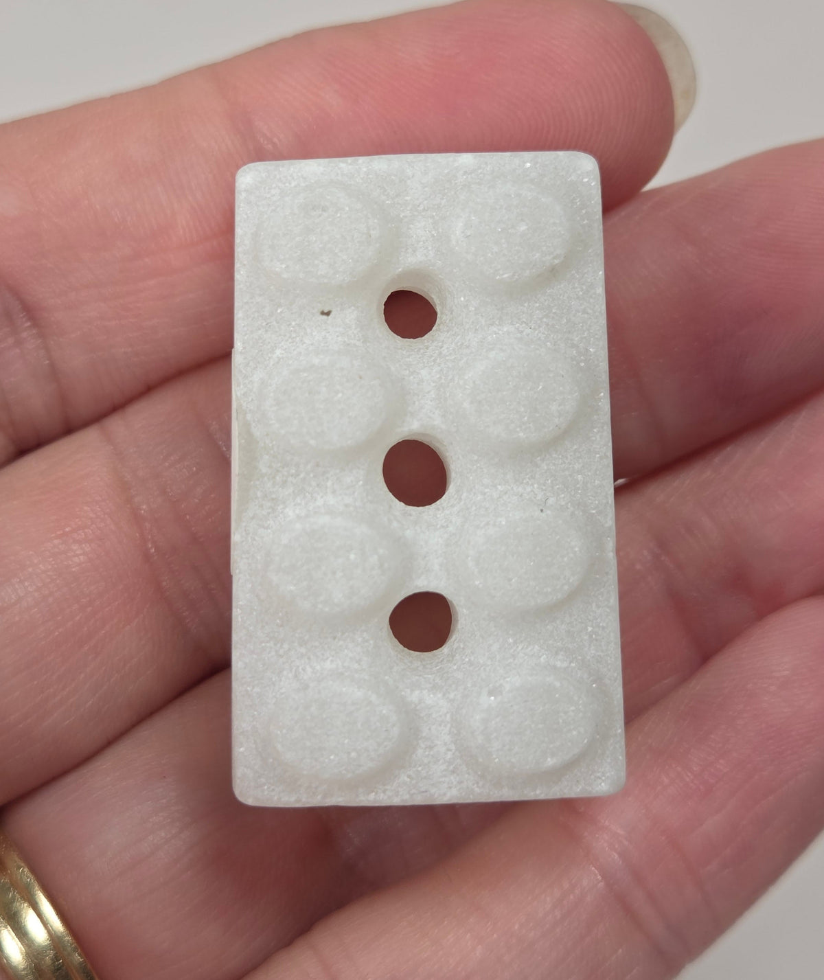 Crystal brick style carving with white coloring being held in a hand against a white background