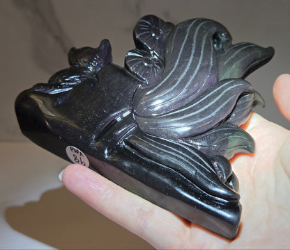 Obsidian stylized fox carving with a light shining highlighting purple coloring being held in a hand against a white marbled background.
