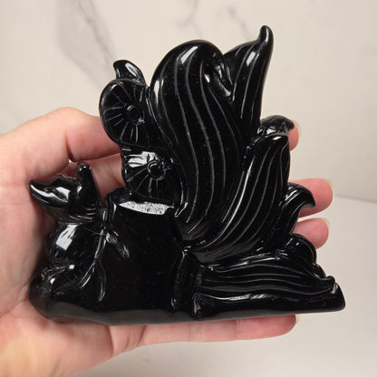 Obsidian stylized fox carving being held in a hand against a white marbled background.