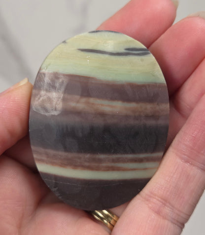 Striped crystal carving in an oval shape being held in a hand against a white background