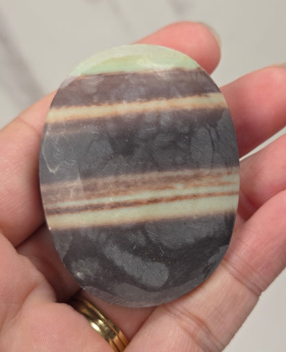 Striped crystal carving in an oval shape being held in a hand against a white background