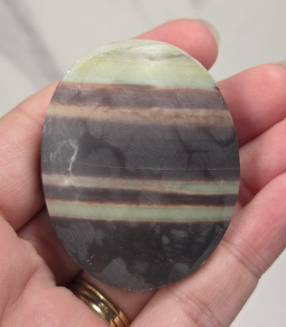 Striped crystal carving in an oval shape being held in a hand against a white background